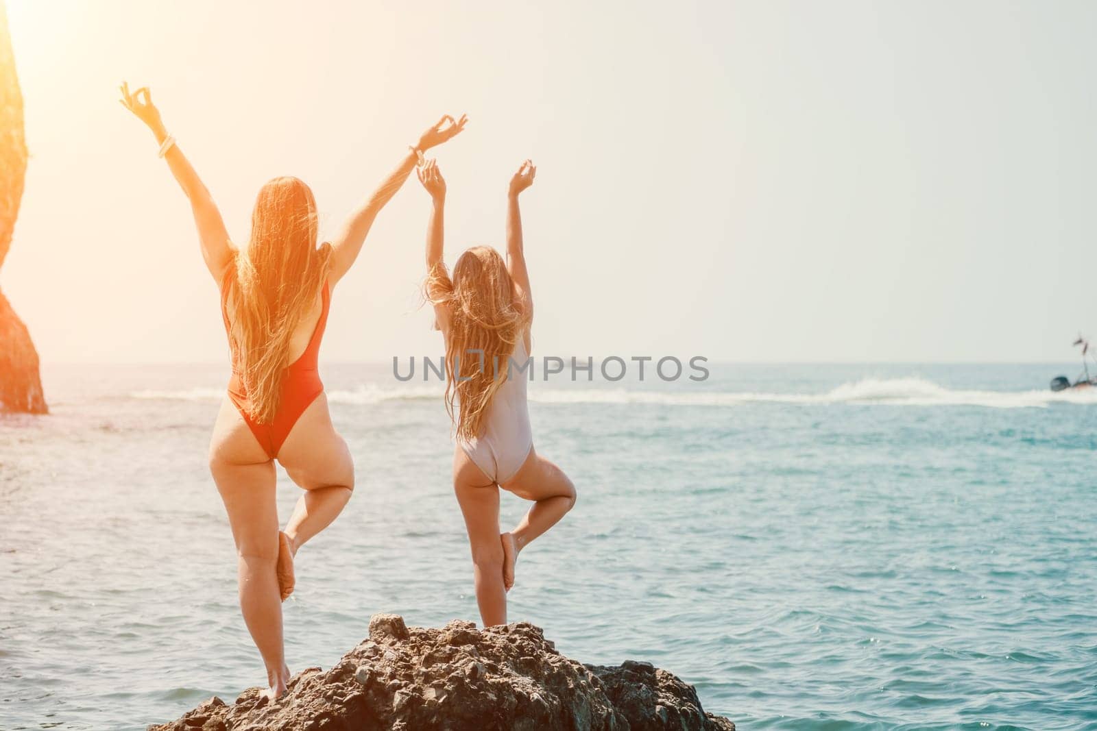 Woman and her daughter practicing balancing yoga pose on one leg up together on rock in the sea. Silhouette mother and daughter doing yoga at beach by panophotograph