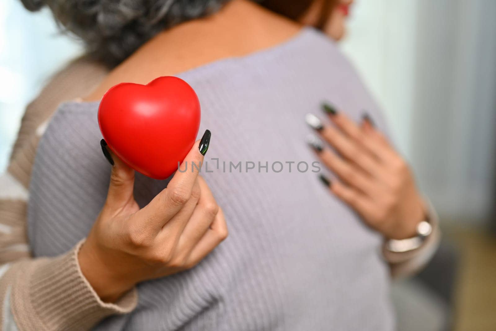 Young woman holding red heart while hugging senior mother . Health care, insurance and world heart day concept.