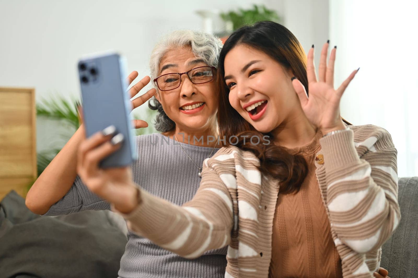 Cheerful young Asian woman taking selfie picture on smartphone with happy mature mother.