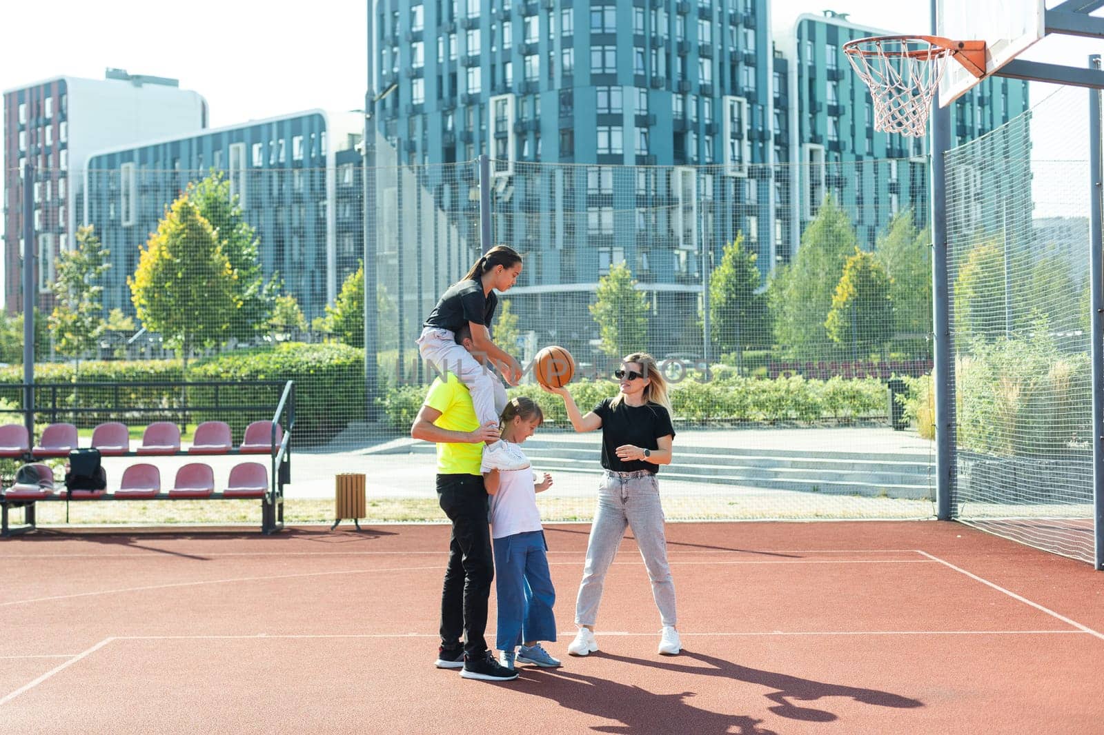 summer holidays, sport and people concept - happy family with ball playing on basketball playground by Andelov13