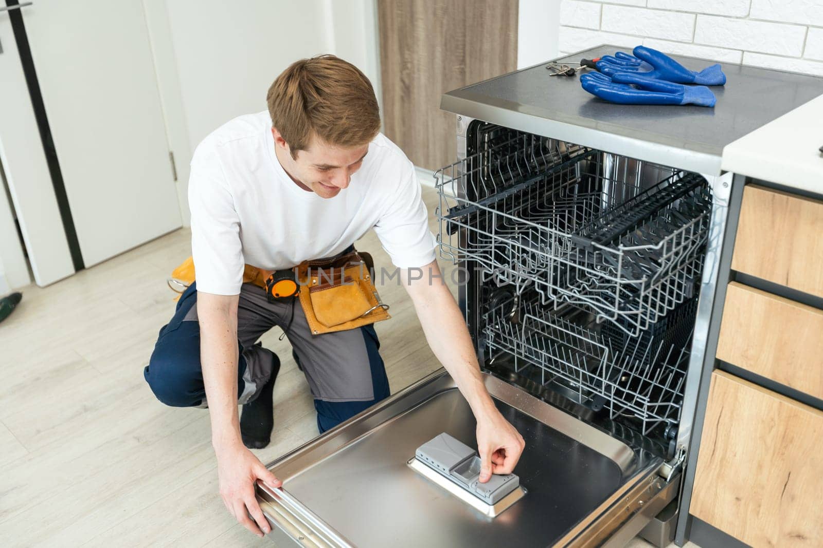 Repairman checks operating state of dishwasher in kitchen.