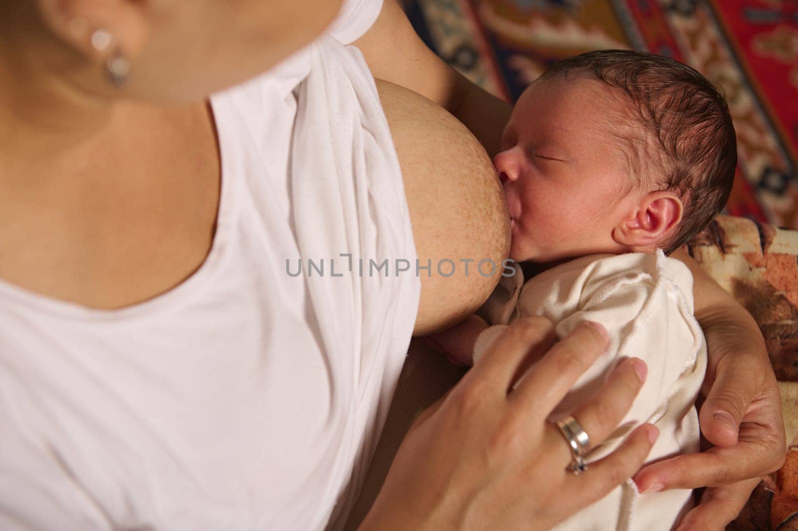 Close-up of a young woman breastfeeding her newborn baby at home by artgf
