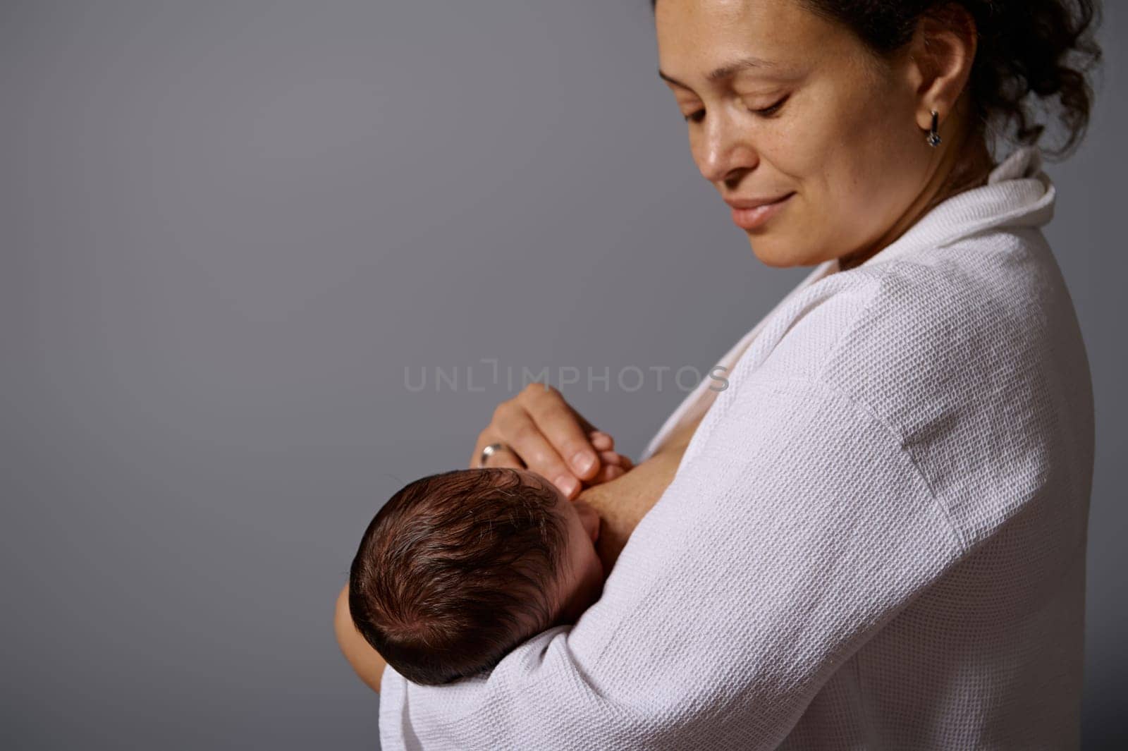 Close up portrait of happy woman, young mother, breastfeeding her newborn baby, isolated gray studio background. Milk from mother's breast is a natural medicine for children. Copying advertising space
