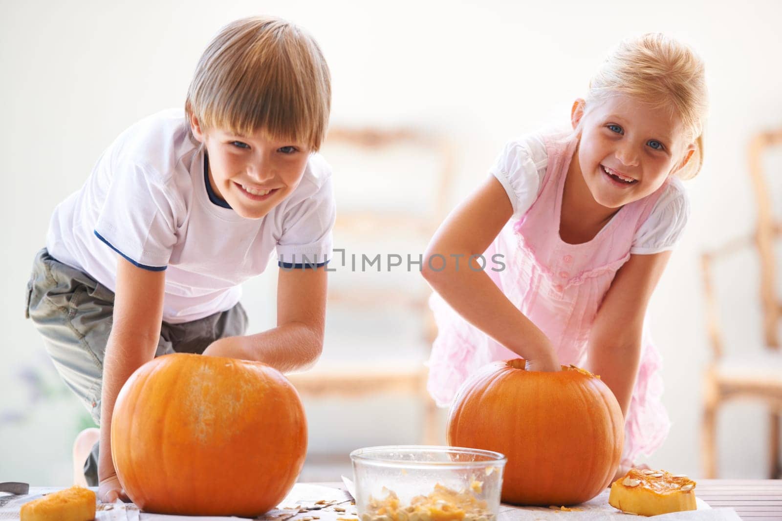Halloween, portrait and carving a pumpkin with children at a home table for fun and bonding. Boy and girl or young kids as siblings together for creativity, holiday lantern and happy craft and play by YuriArcurs