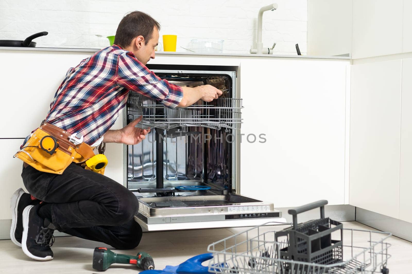 Male Technician Examining Dishwasher With Digital Multimeter by Andelov13