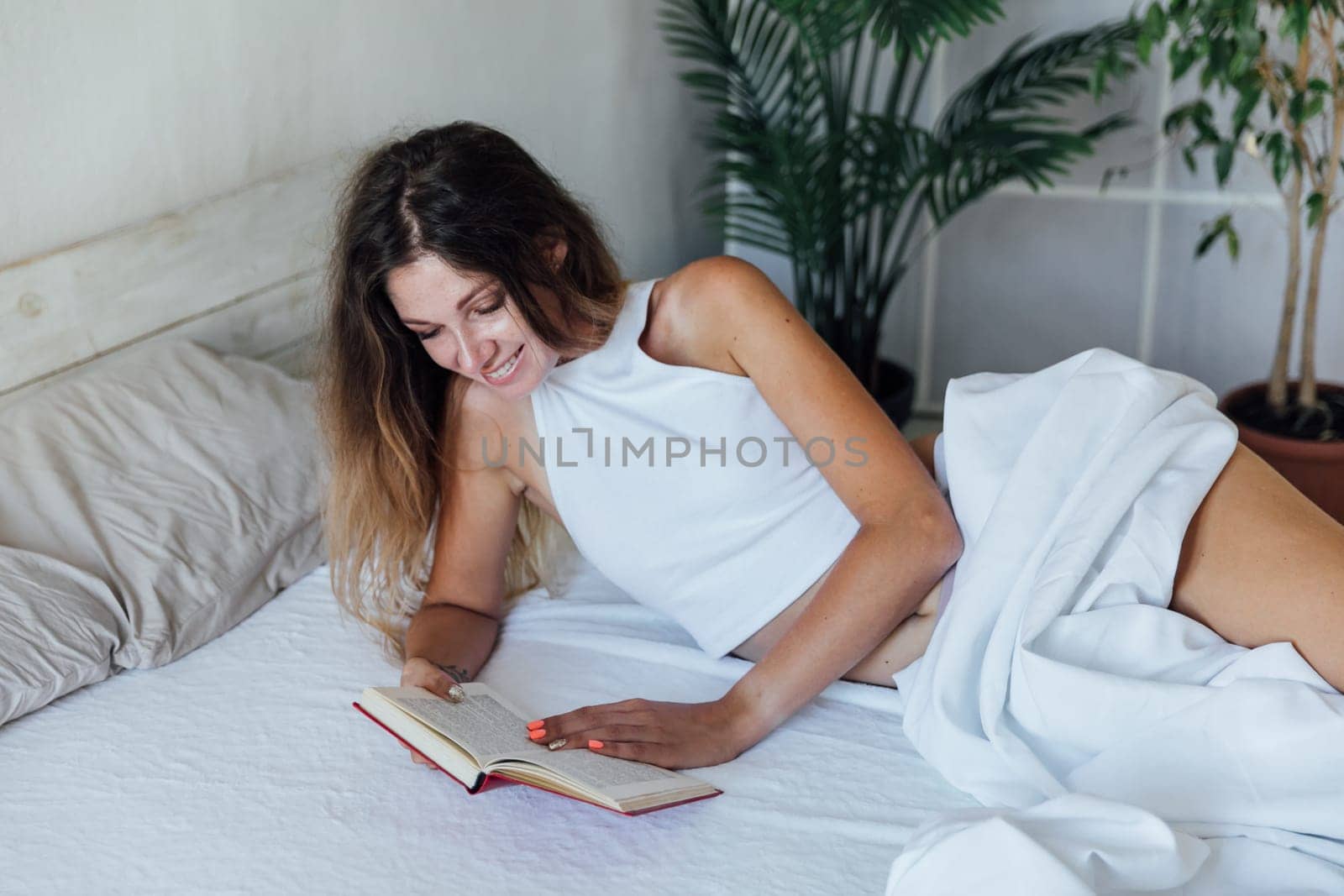 Beautiful woman reading a book in the bedroom on the bed by Simakov