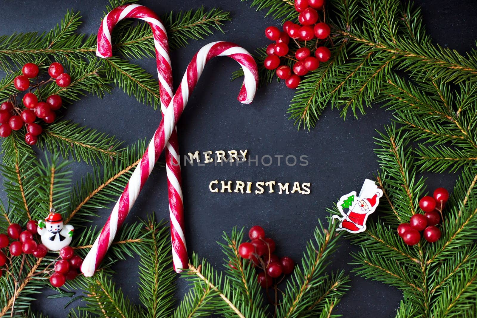 Candy on black background with branches of trees. The inscription Merry Christmas.