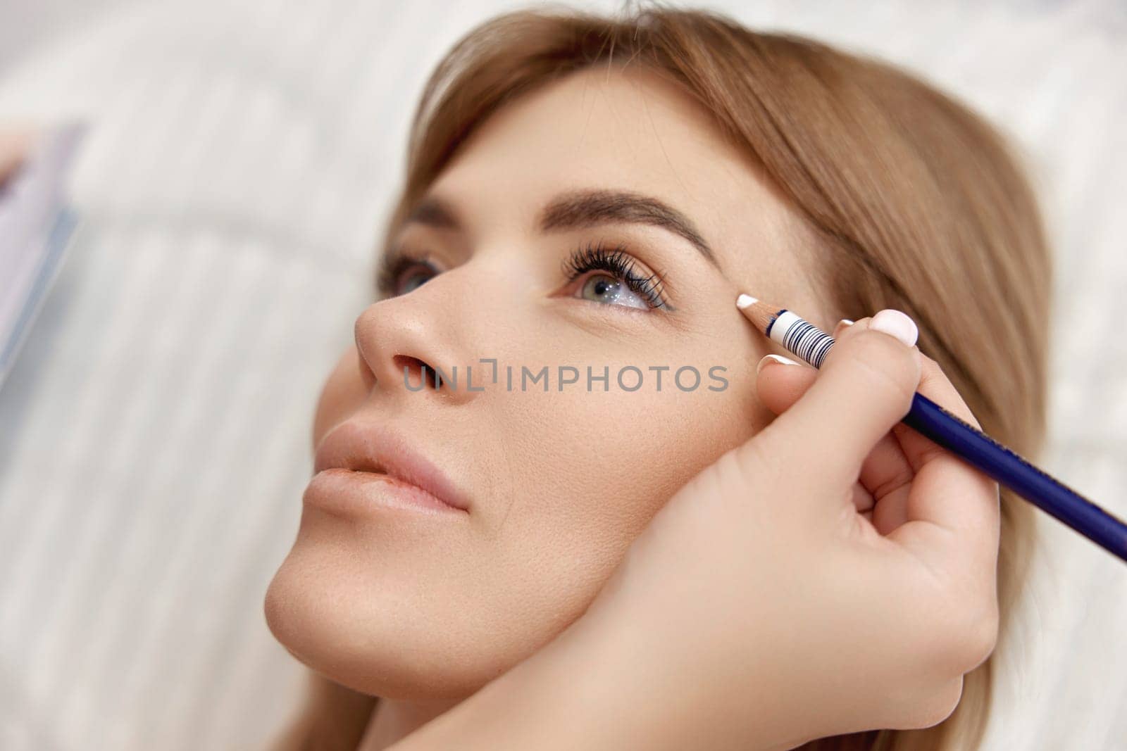 cosmetologist marking skin of caucasian woman with white pencil. facial marking for aesthetic procedure.