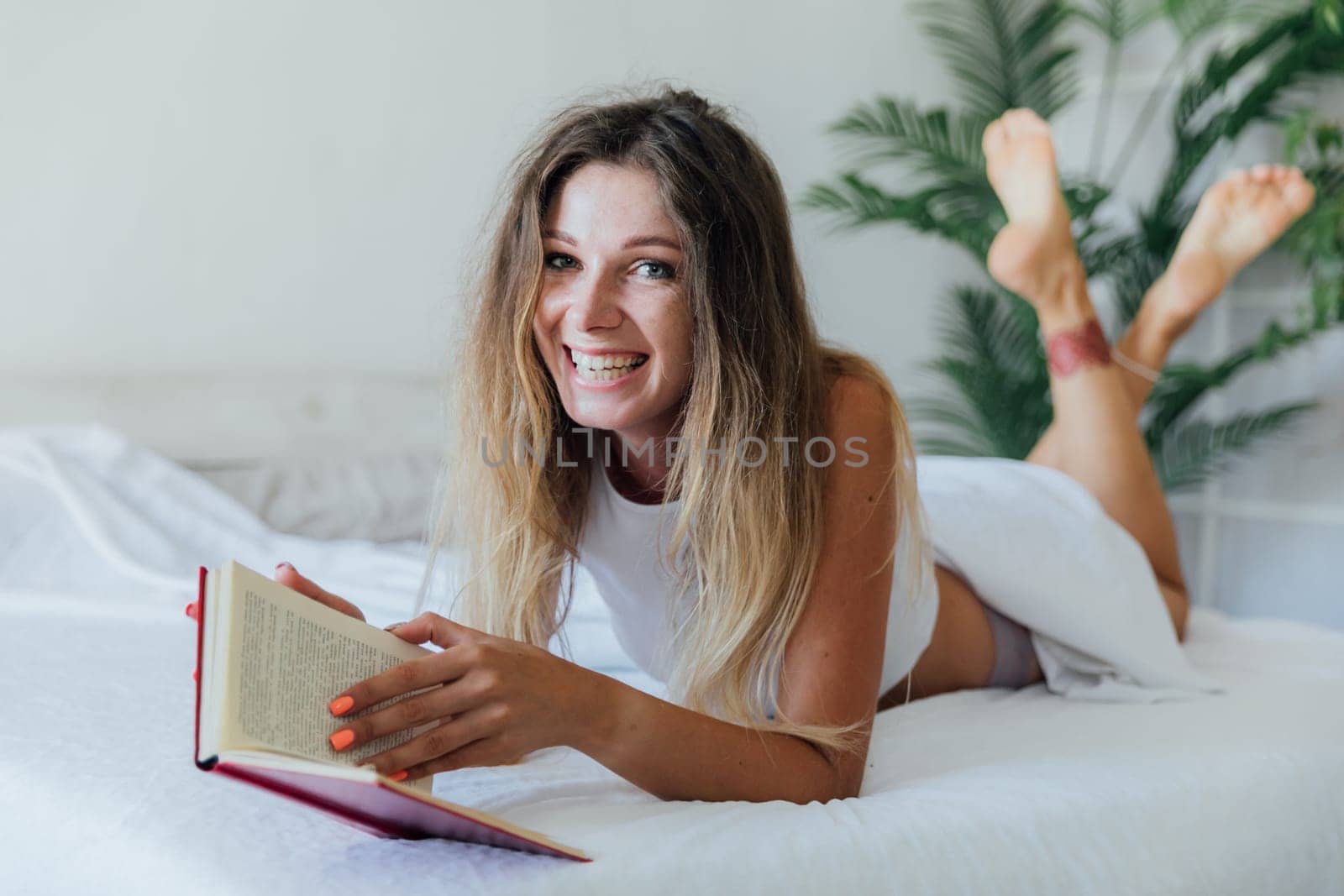 Cute lovely young woman reading book and drinking coffee on bed by Simakov