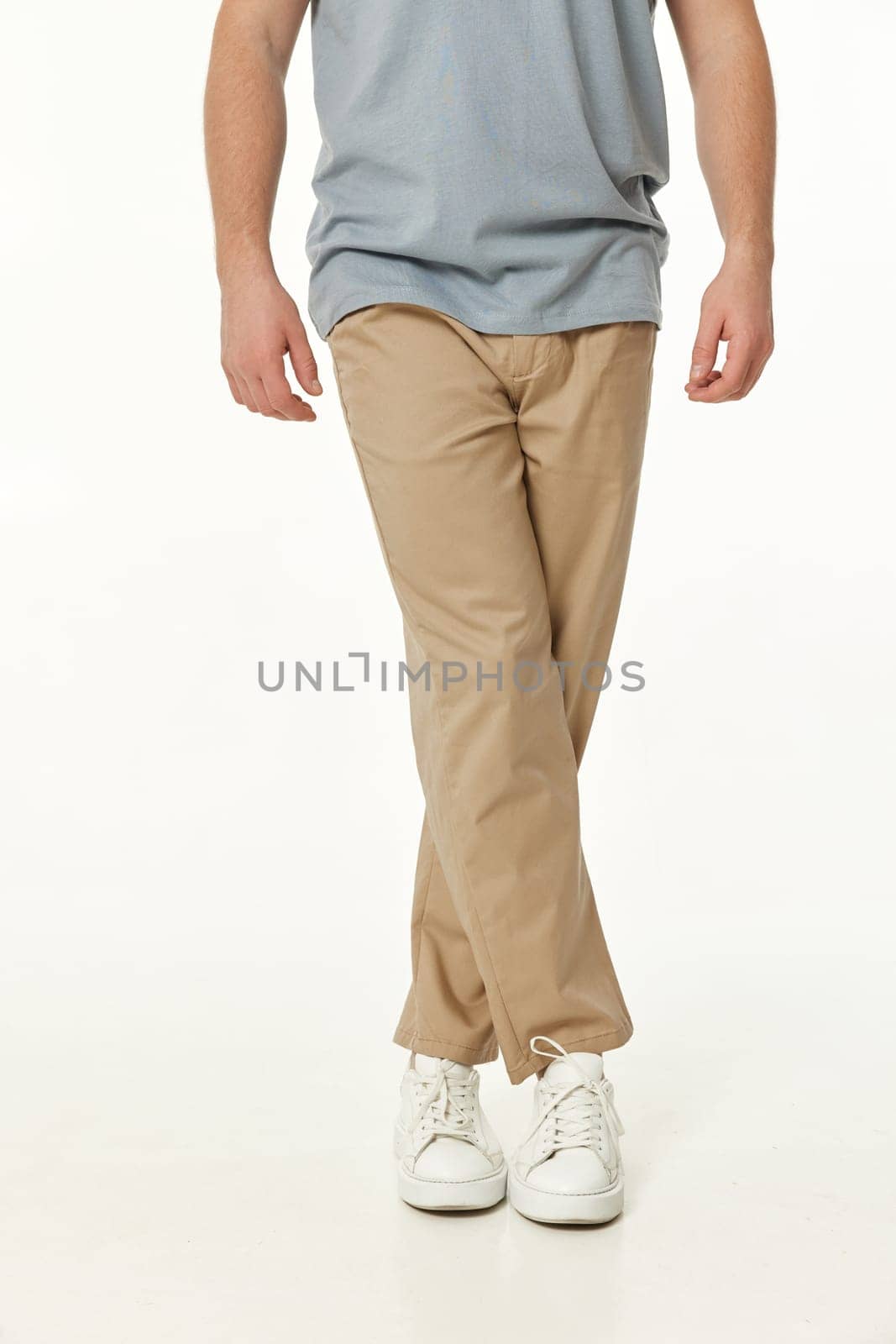 guy with crossed legs. man wearing white sneakers and casual beige pants on studio background