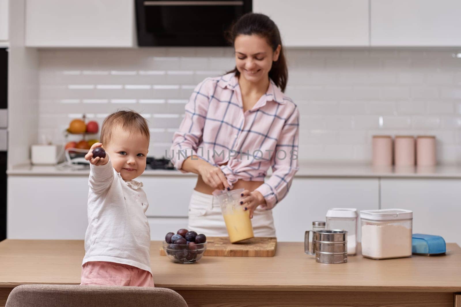 mother with her little daughter preparing plum pie at kitchen. baking together