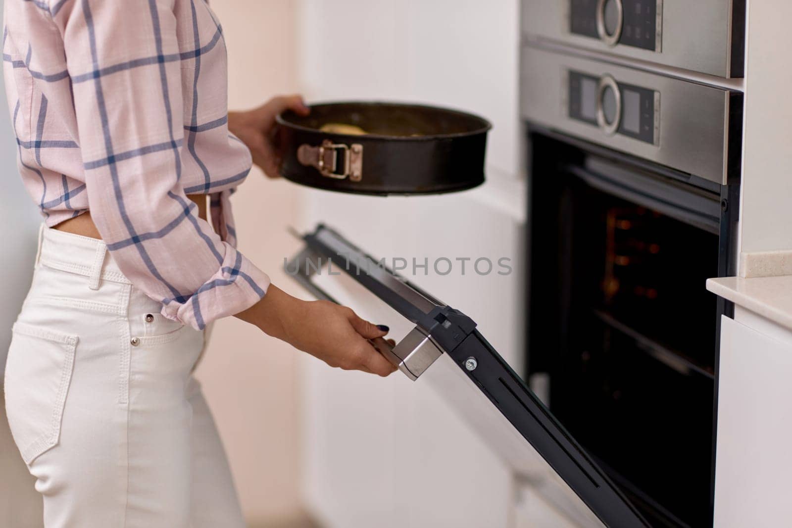 female hands put pan of plum dough into the modern kitchen oven.