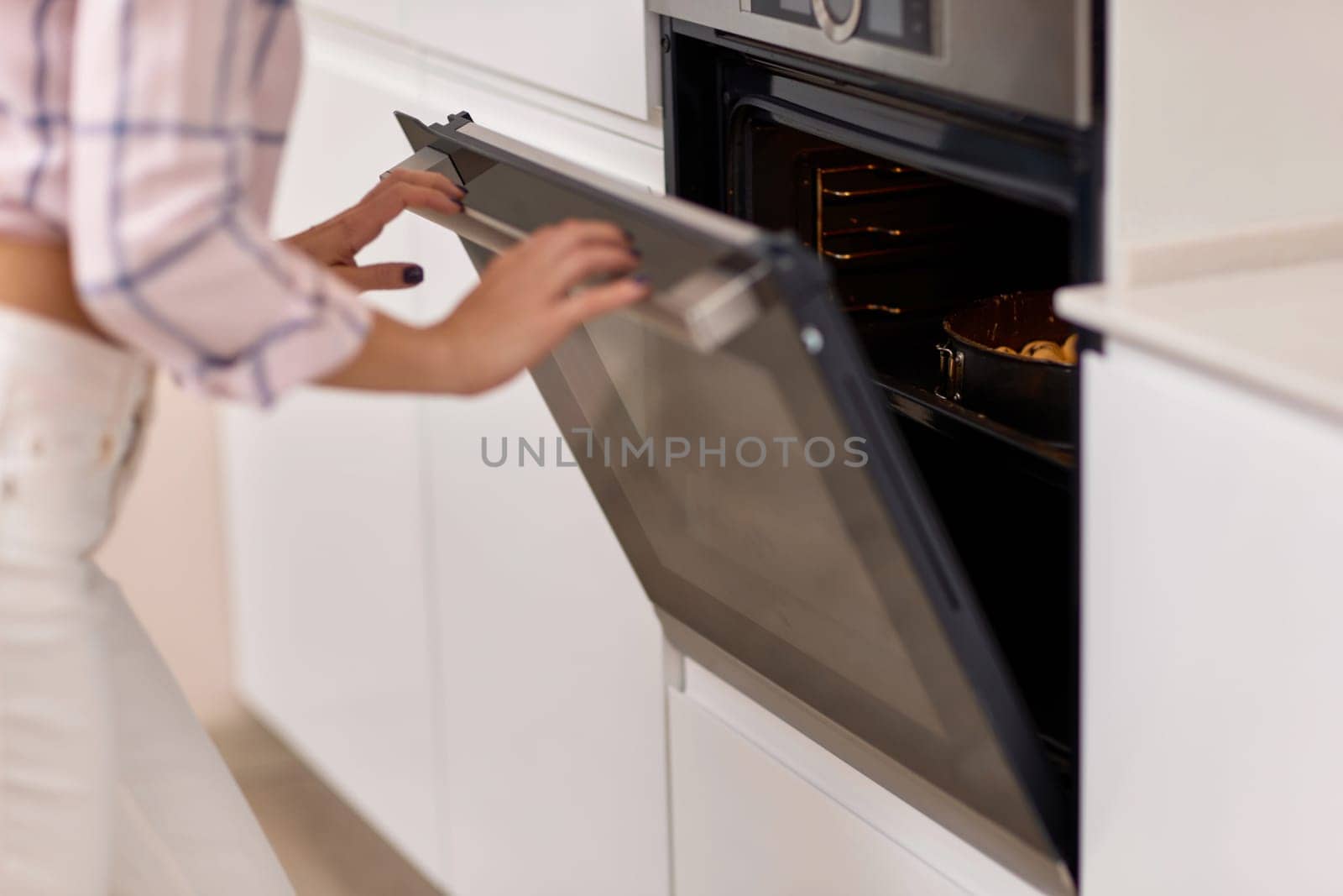 female hands put pan of plum dough into the modern kitchen oven.