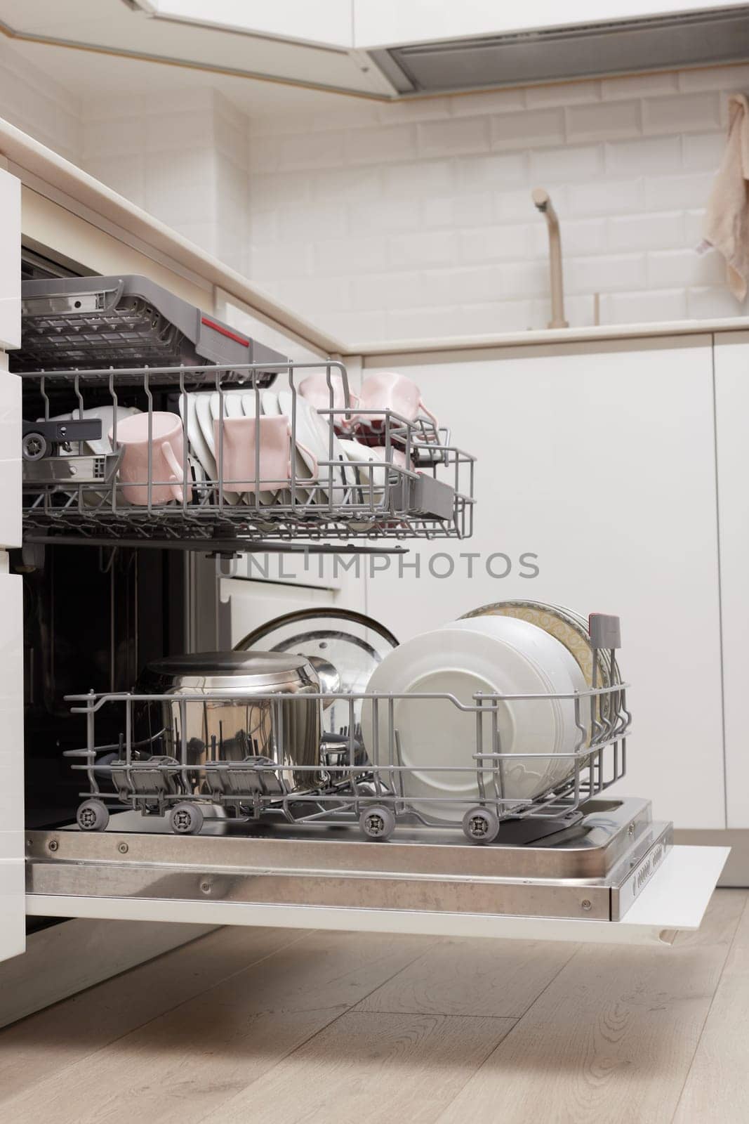 Open built-in dishwasher machine with clean cutlery, dishes, plates in white modern kitchen. side view