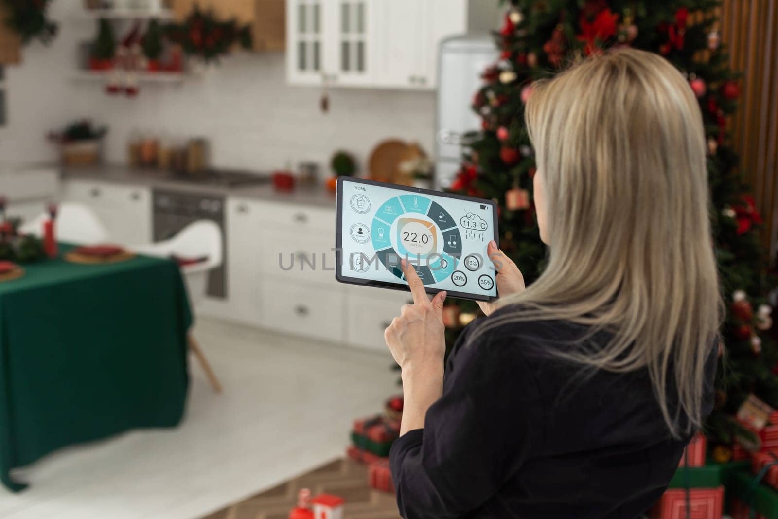 Woman pushing button on kitchen app of smart home on digital tablet at home. Concept of modern home control. Idea of domestic lifestyle. Cropped image of girl. Blurred man on background using laptop