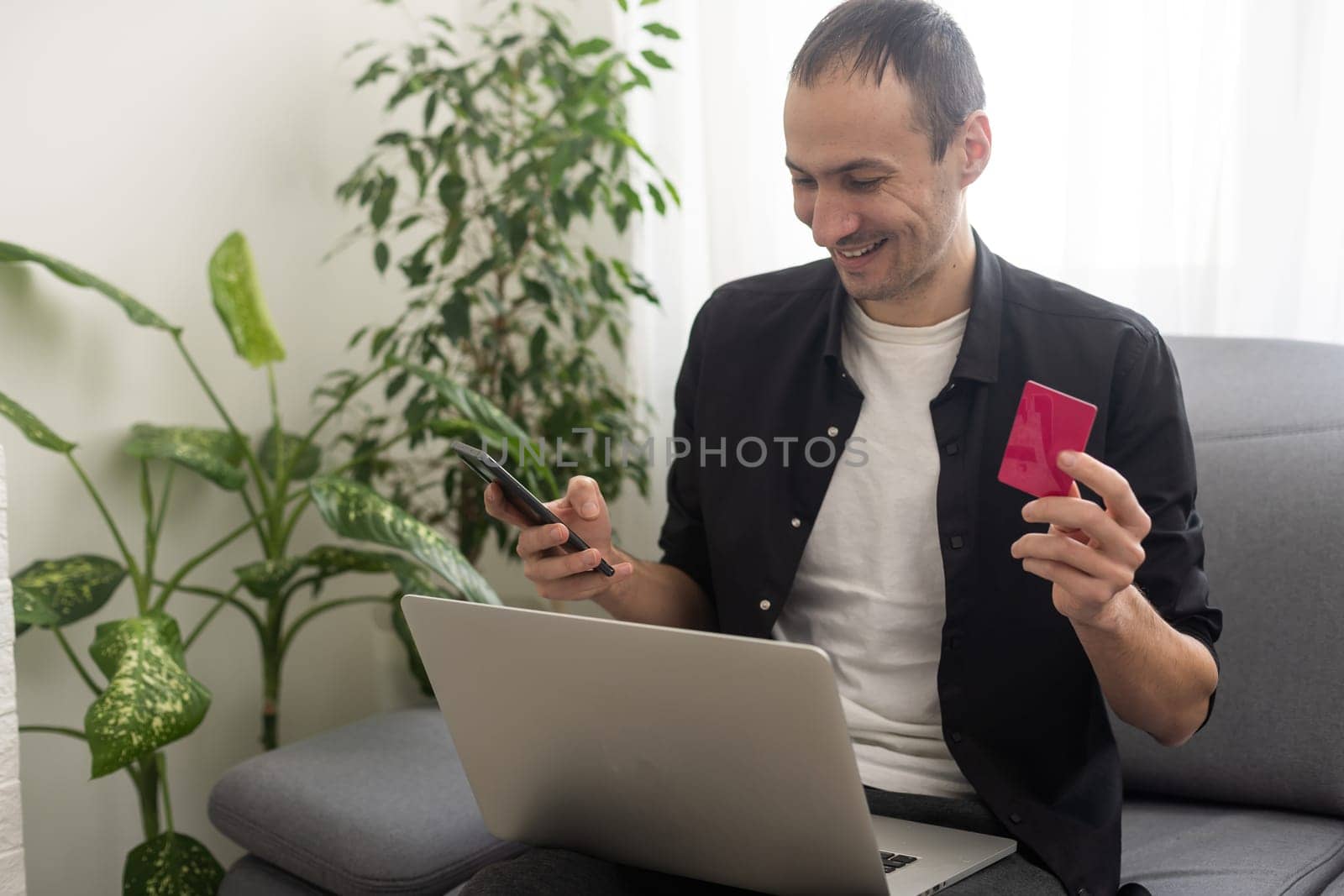Smiling man sitting in office and pays by credit card with his mobile phone