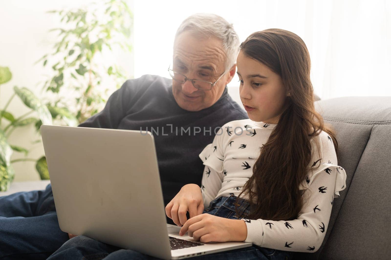 Adorable little girl and happy grandfather using laptop at home by Andelov13