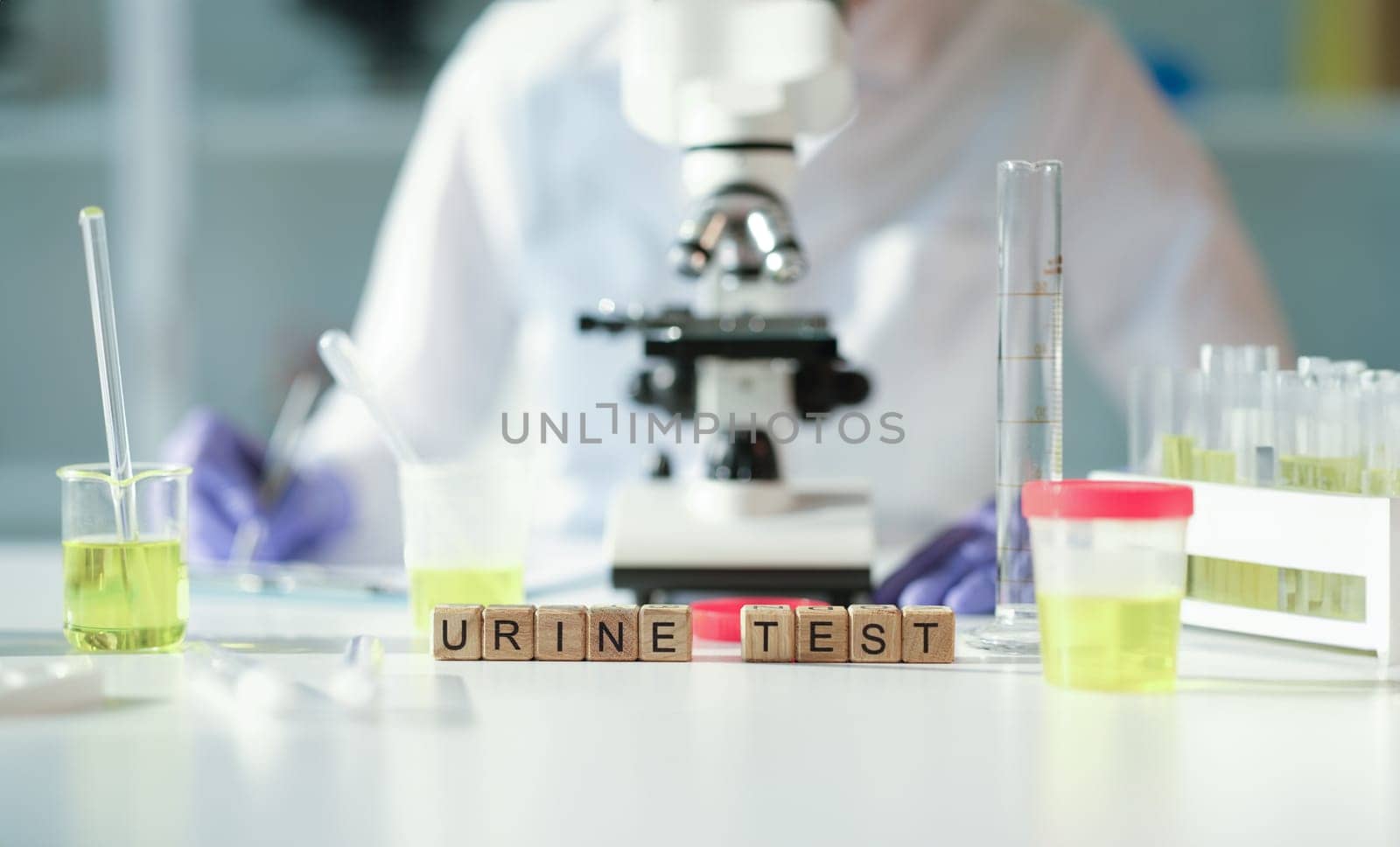 Word urine test on wooden cubes against background of microscope and jars in lab closeup. Laboratory diagnosis of diseases of urinary system concept