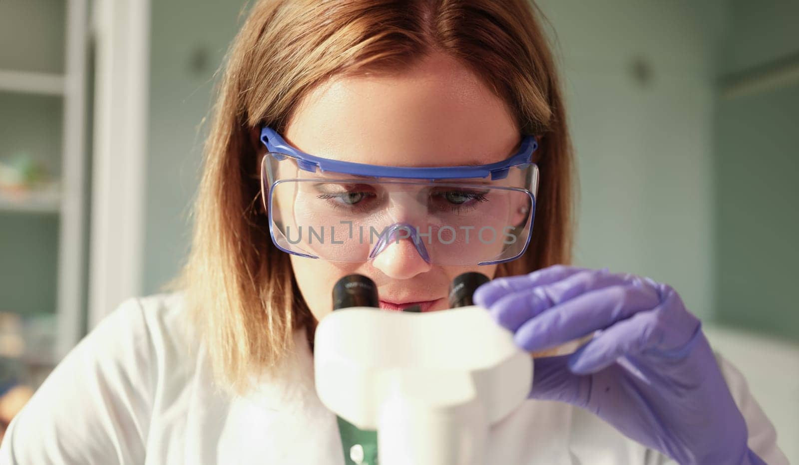 Scientist chemist in protective glasses looking through microscope in chemical lab. Laboratory medical blood tests concept