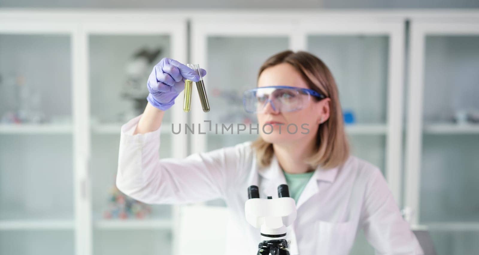 Woman scientist chemist comparing test tubes with oil and contaminated diesel fuel in lab. Quality control of petroleum products concept