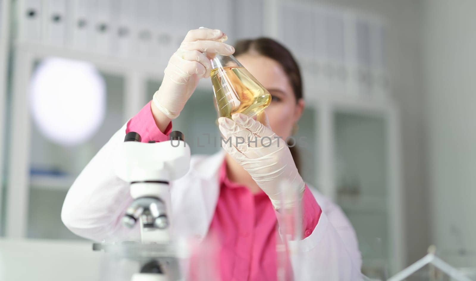 Scientist chemist looking at flask with yellow brake oil in chemistry lab closeup by kuprevich