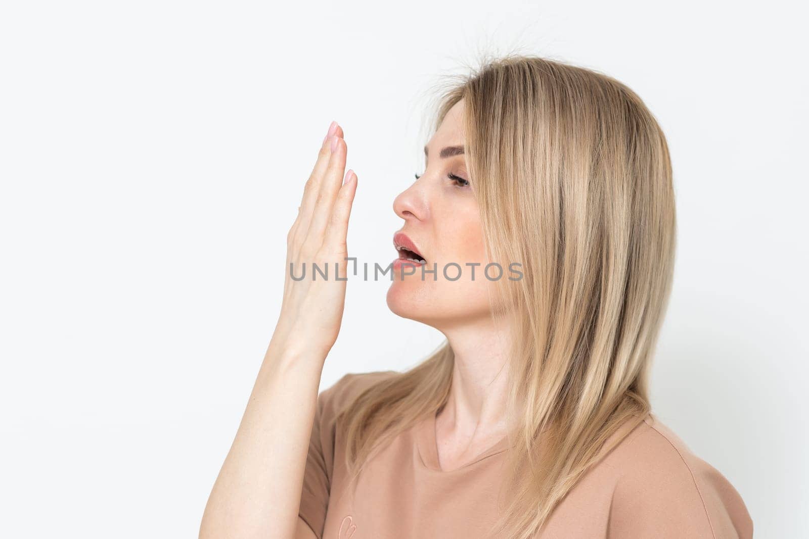 Health Care: Woman checking her breath with hand. Closeup portrait headshot sleepy young woman with wide open mouth