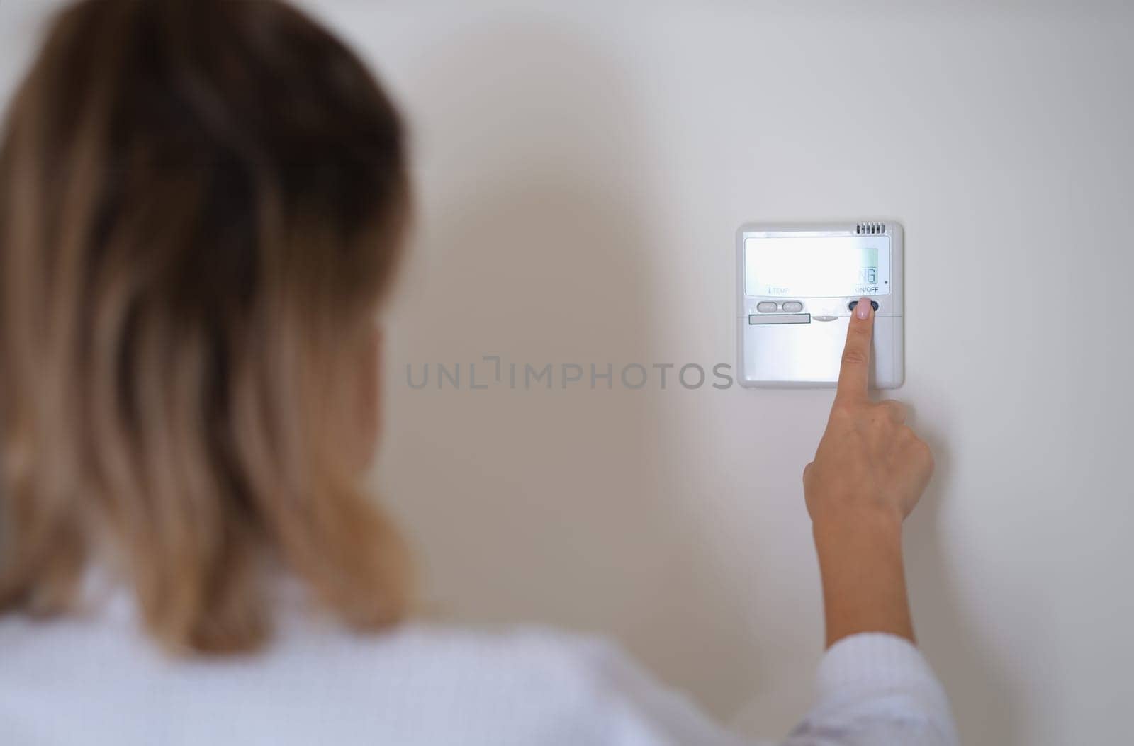 Woman pressing button on remote control of air conditioner in wall closeup by kuprevich