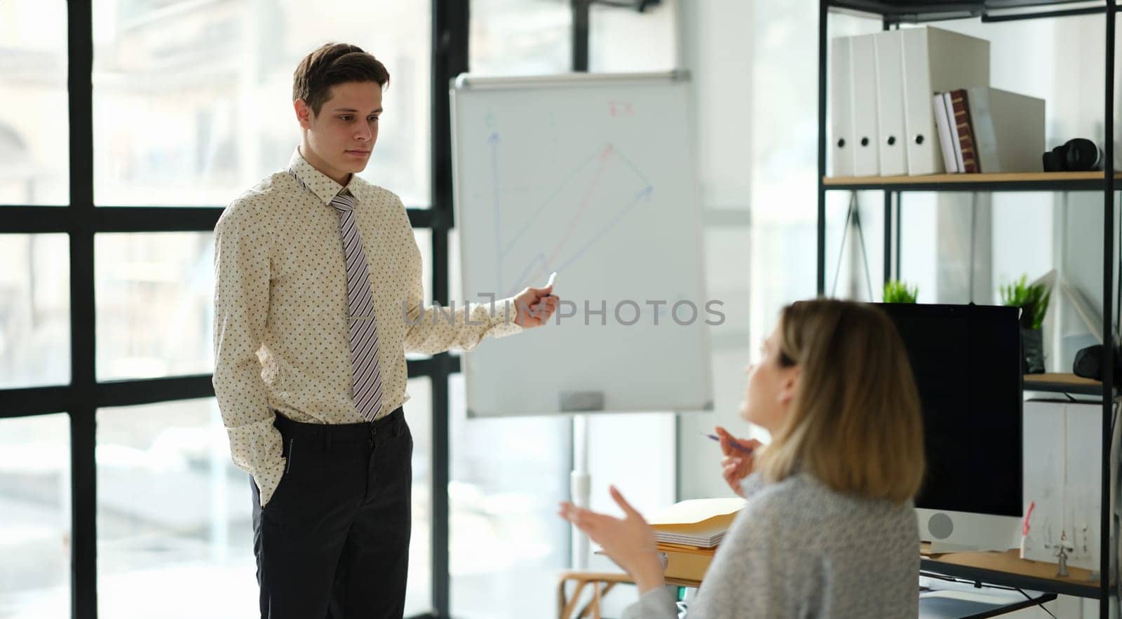 Business coach showing charts on blackboard to student in office. Business education concept