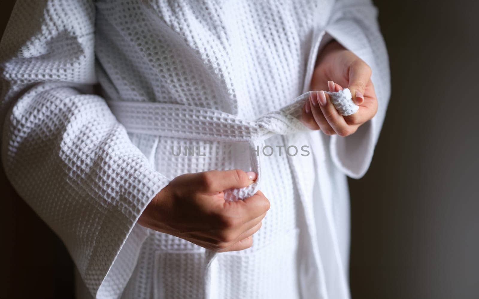 Women hands tying belt on white bathrobe closeup. Comfortable clothes for home concept