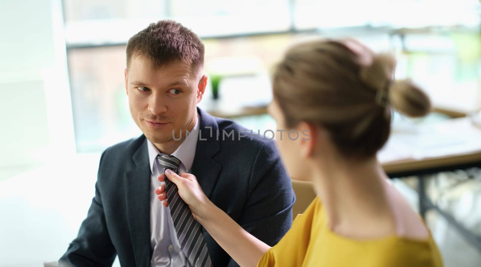 Woman secretary straightening tie to manager man at work in office by kuprevich