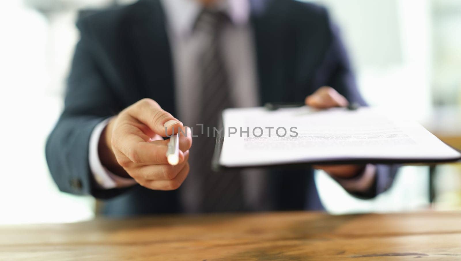 Manager holding out paper document on clipboard and pen for signing closeup by kuprevich