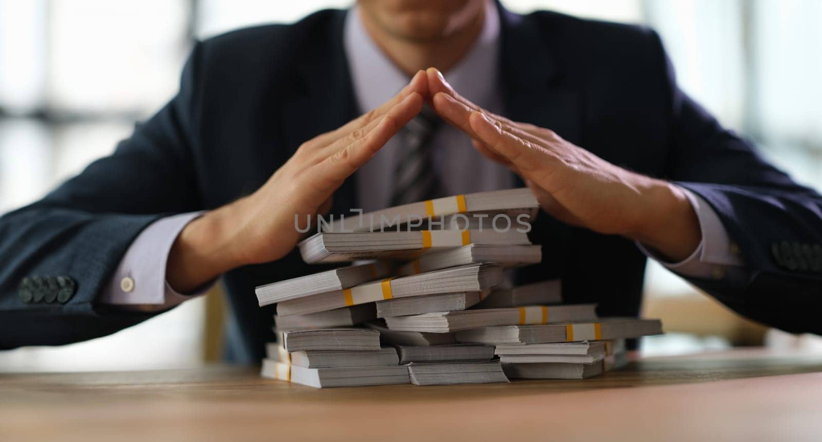 Businessman banker making roof over stacks of money with hands closeup by kuprevich