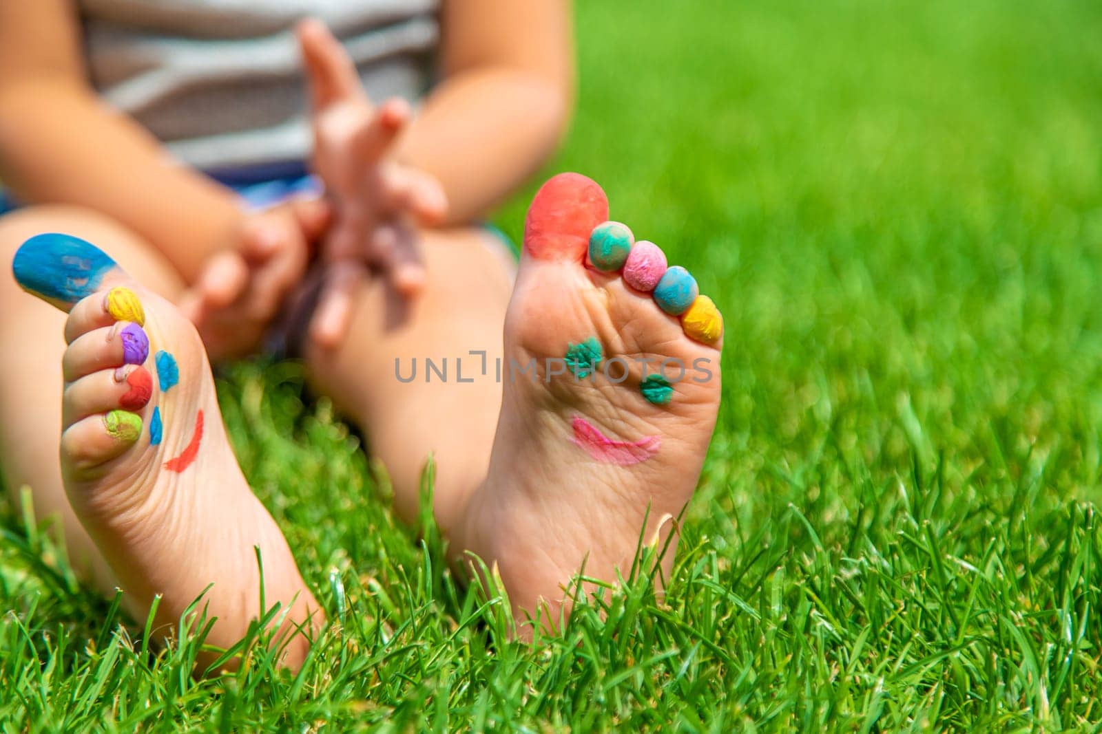 Child feet drawing smile in the park on the grass. Selective focus. Kid.