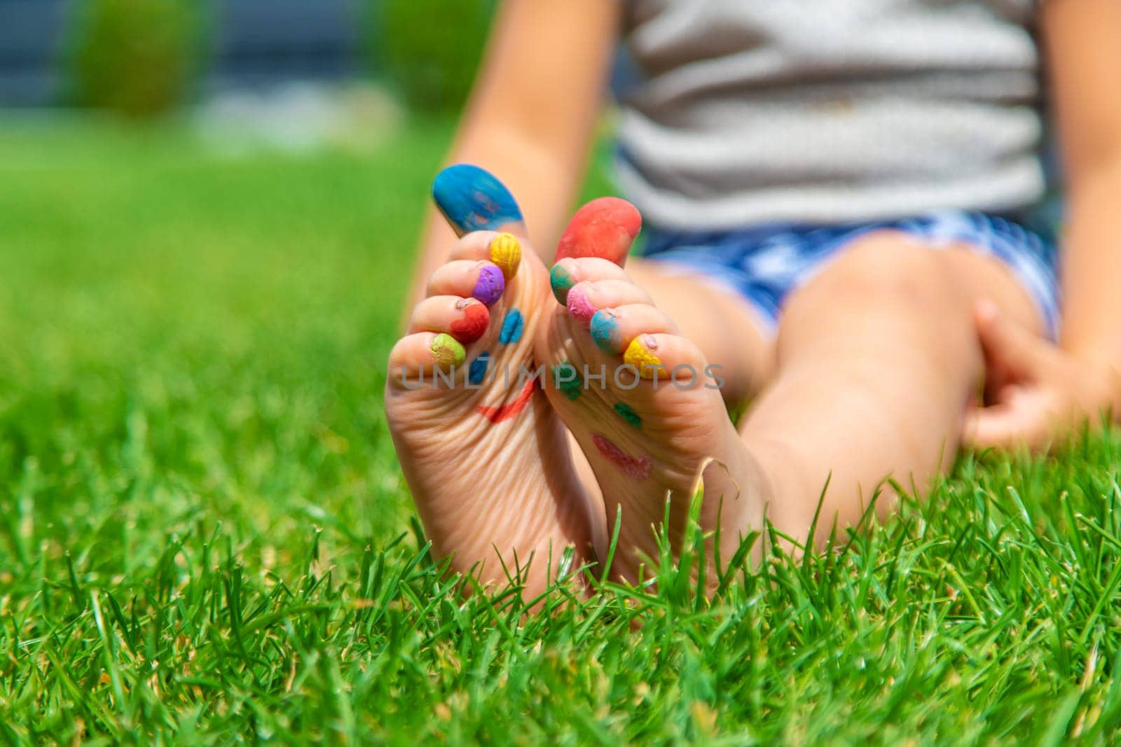 Child feet drawing smile in the park on the grass. Selective focus. by yanadjana