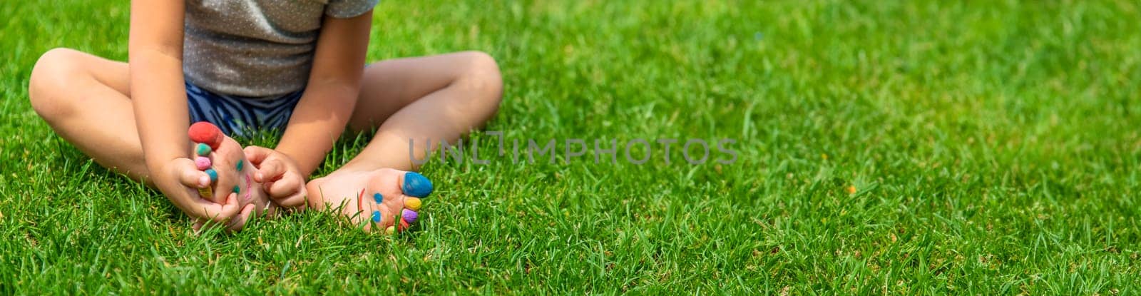 Child feet drawing smile in the park on the grass. Selective focus. Kid.