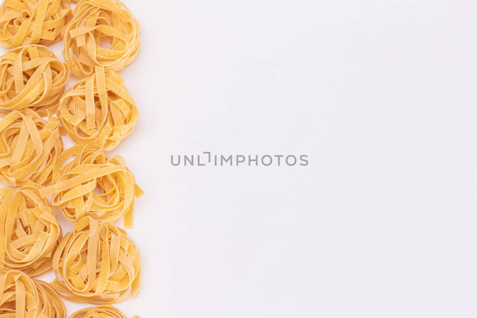 Classic Italian Raw Egg Fettuccine with Copy Spase on White Background. Dry Twisted Uncooked Pasta. Italian Culture and Cuisine. Raw Golden Macaroni Pattern