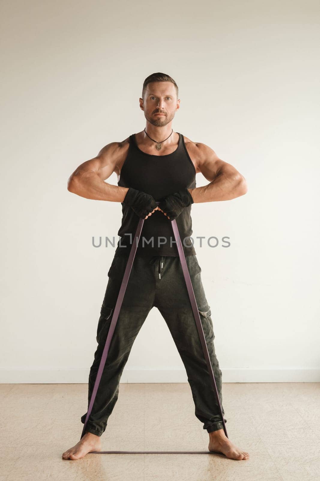 A man in black sportswear is engaged in strength fitness using a rubber loop indoors.