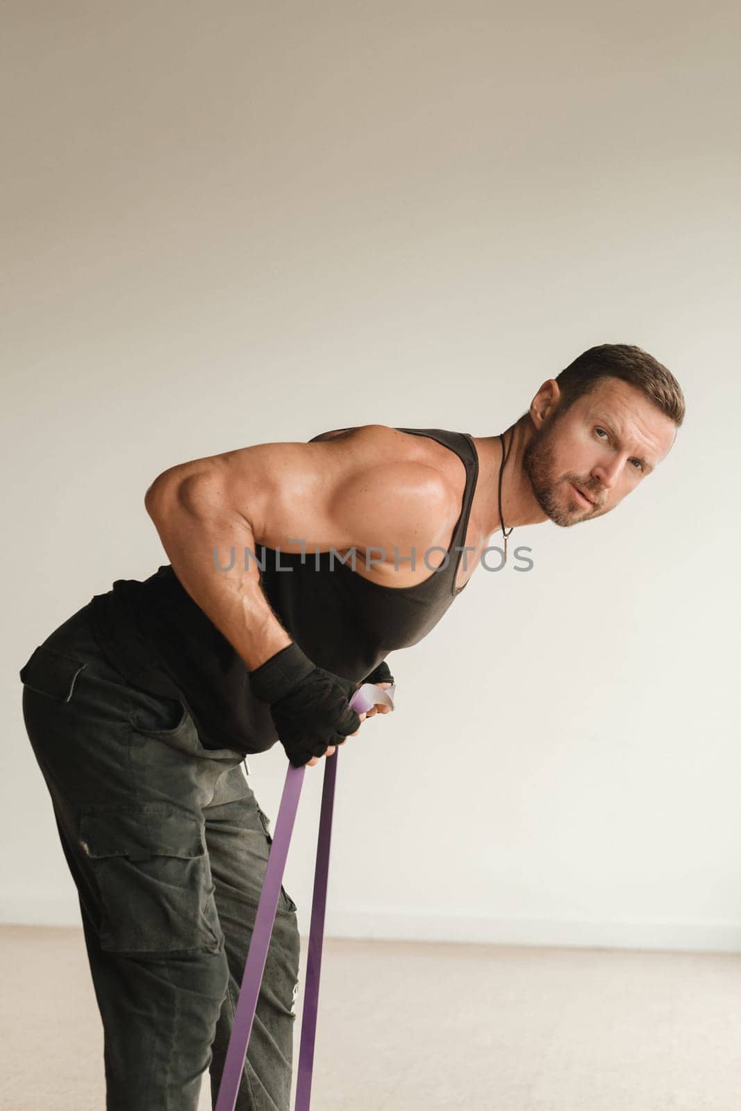 A man in black sportswear is engaged in strength fitness using a rubber loop indoors.