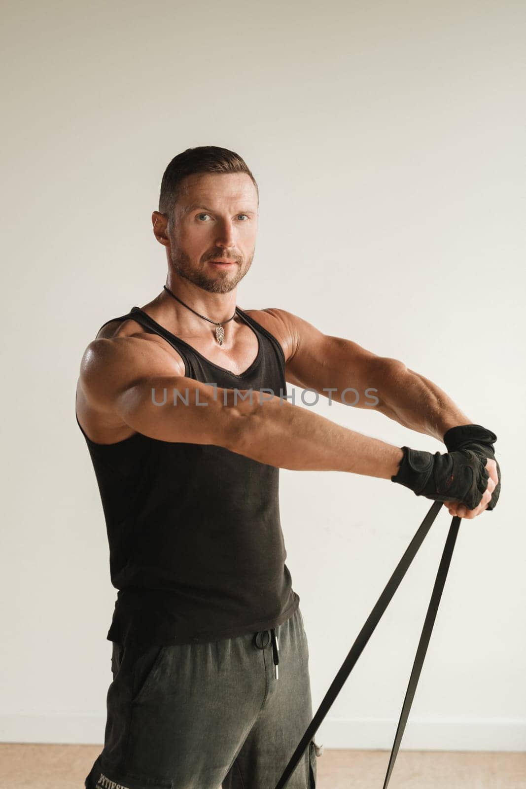 A man in black sportswear is engaged in strength fitness using a rubber loop indoors.