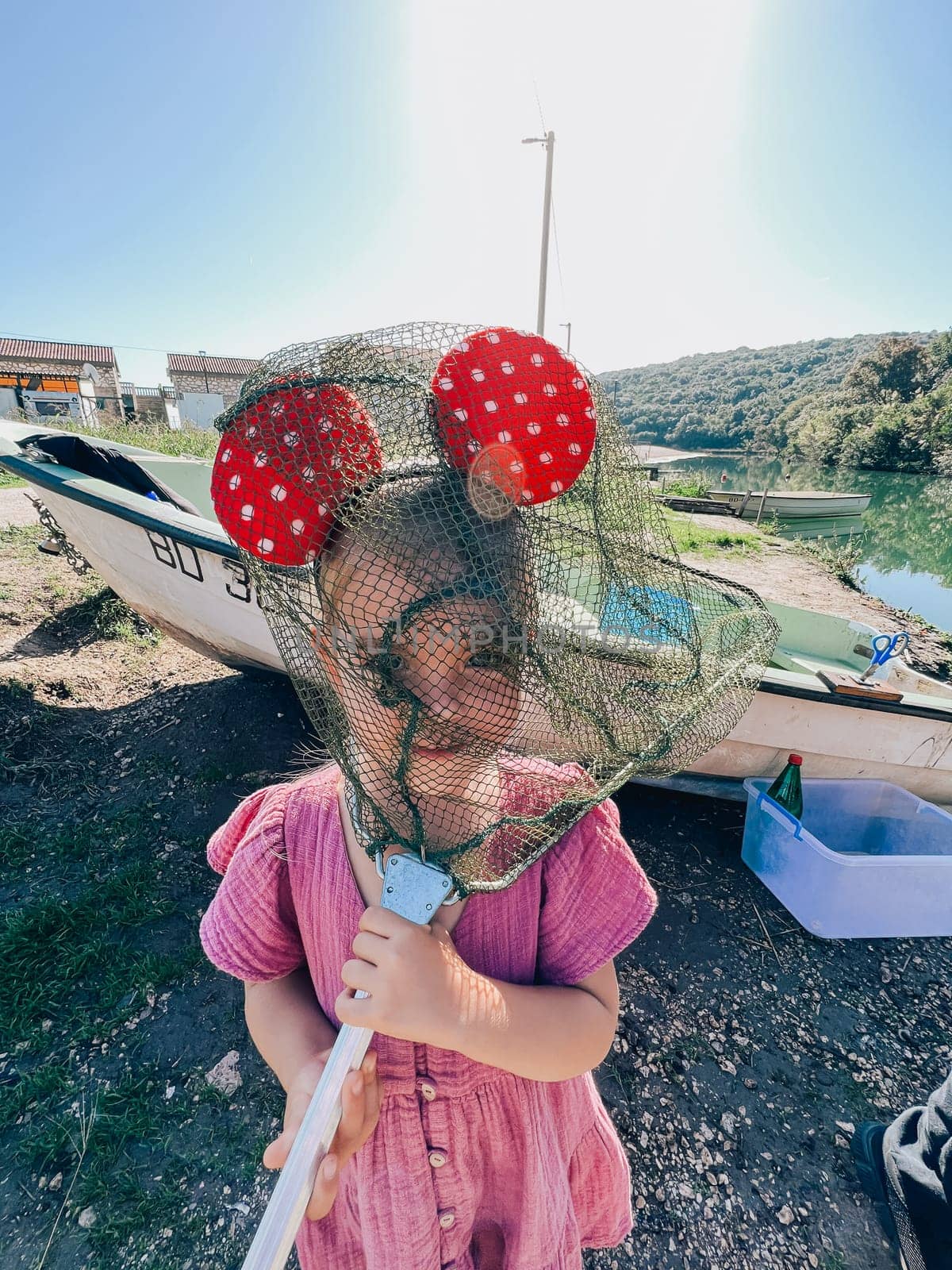 Little girl with Minnie Mouse ears on her head hides behind a fishing net on the shore. High quality photo