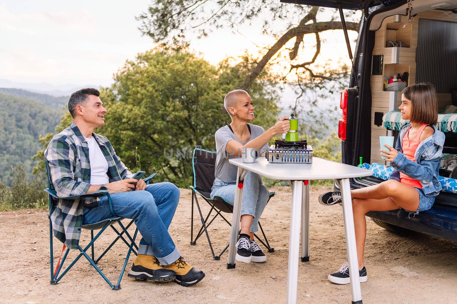 family having breakfast in the countryside next to their camper van, concept of active tourism in nature and outdoor activities with children