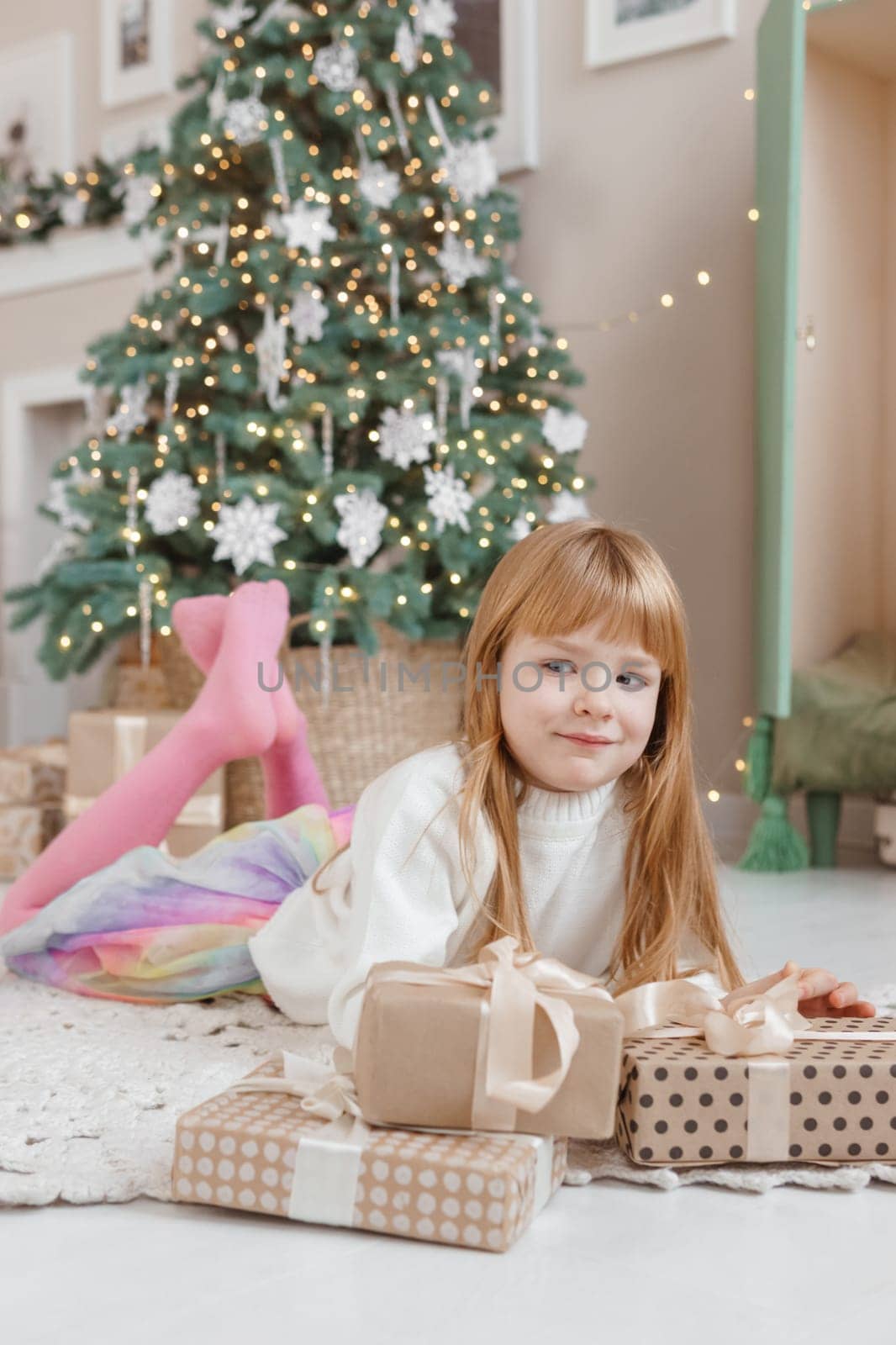 A little red-haired girl lies next to Christmas gifts in a craft package. Happy Christmas concept