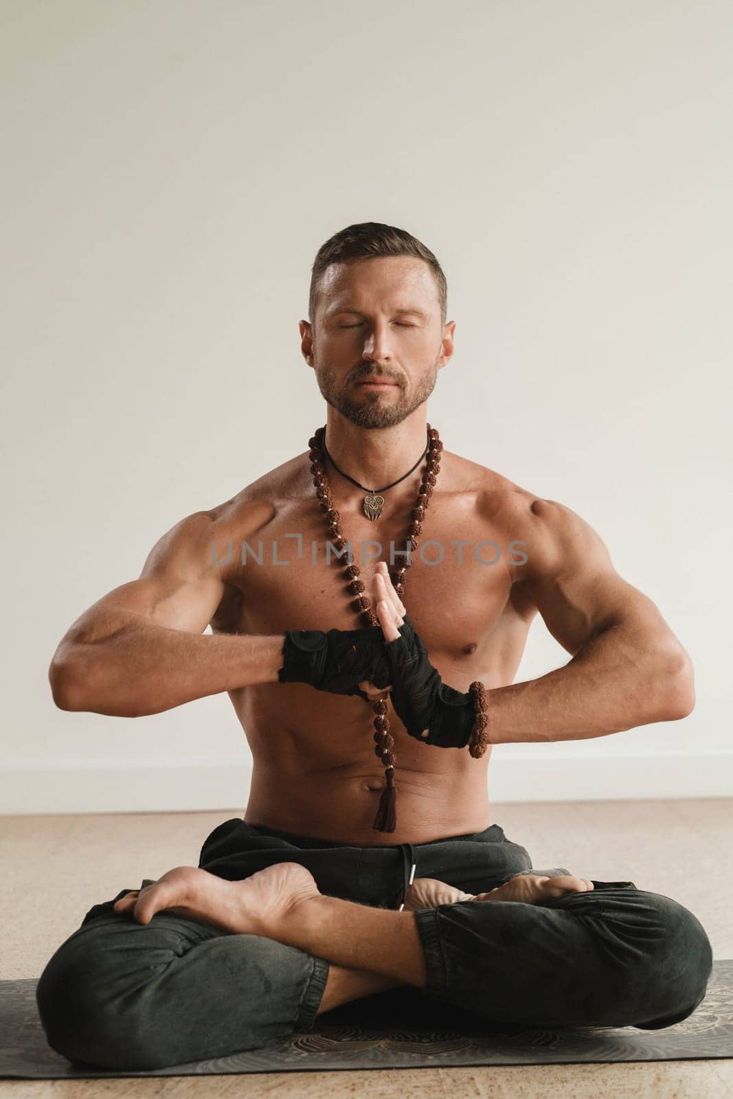 a man with a naked torso is sitting in the lotus position before doing yoga indoors. Fitness Trainer.