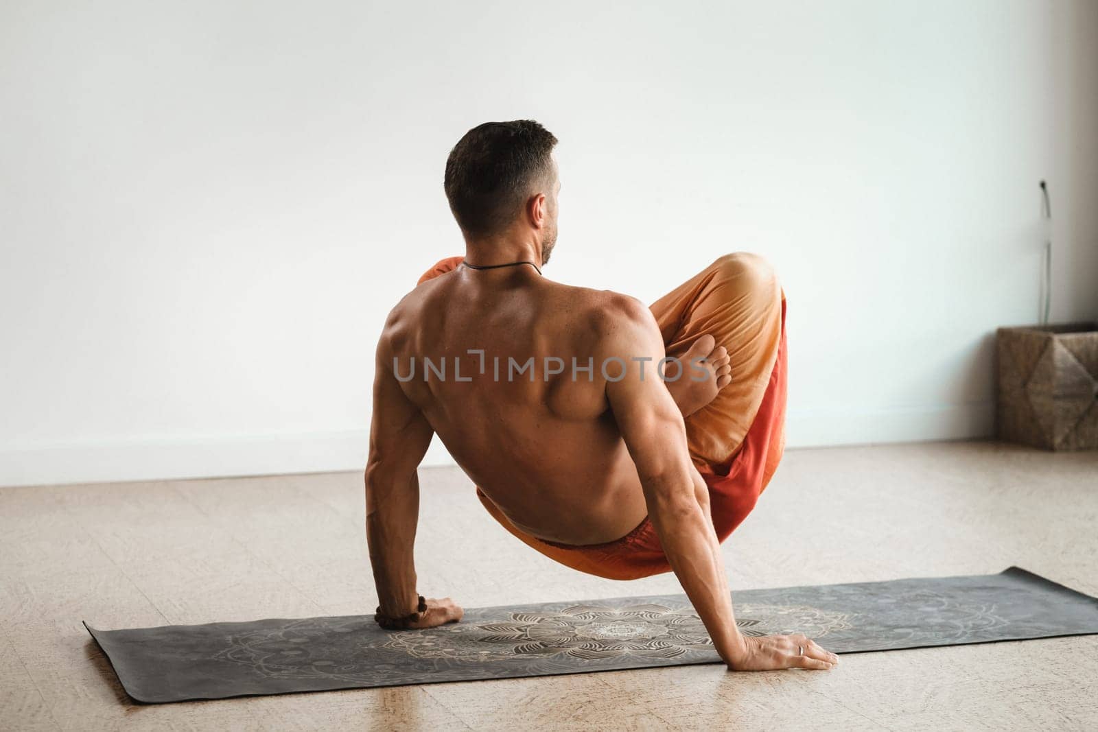 a man with a naked torso does yoga standing on his hands indoors. Fitness Trainer.