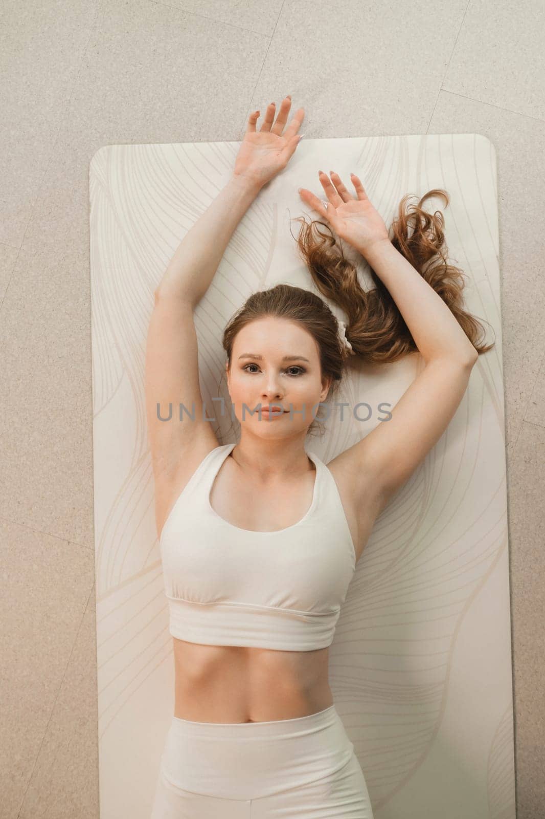 A girl in white clothes does yoga lying on a rug indoors.