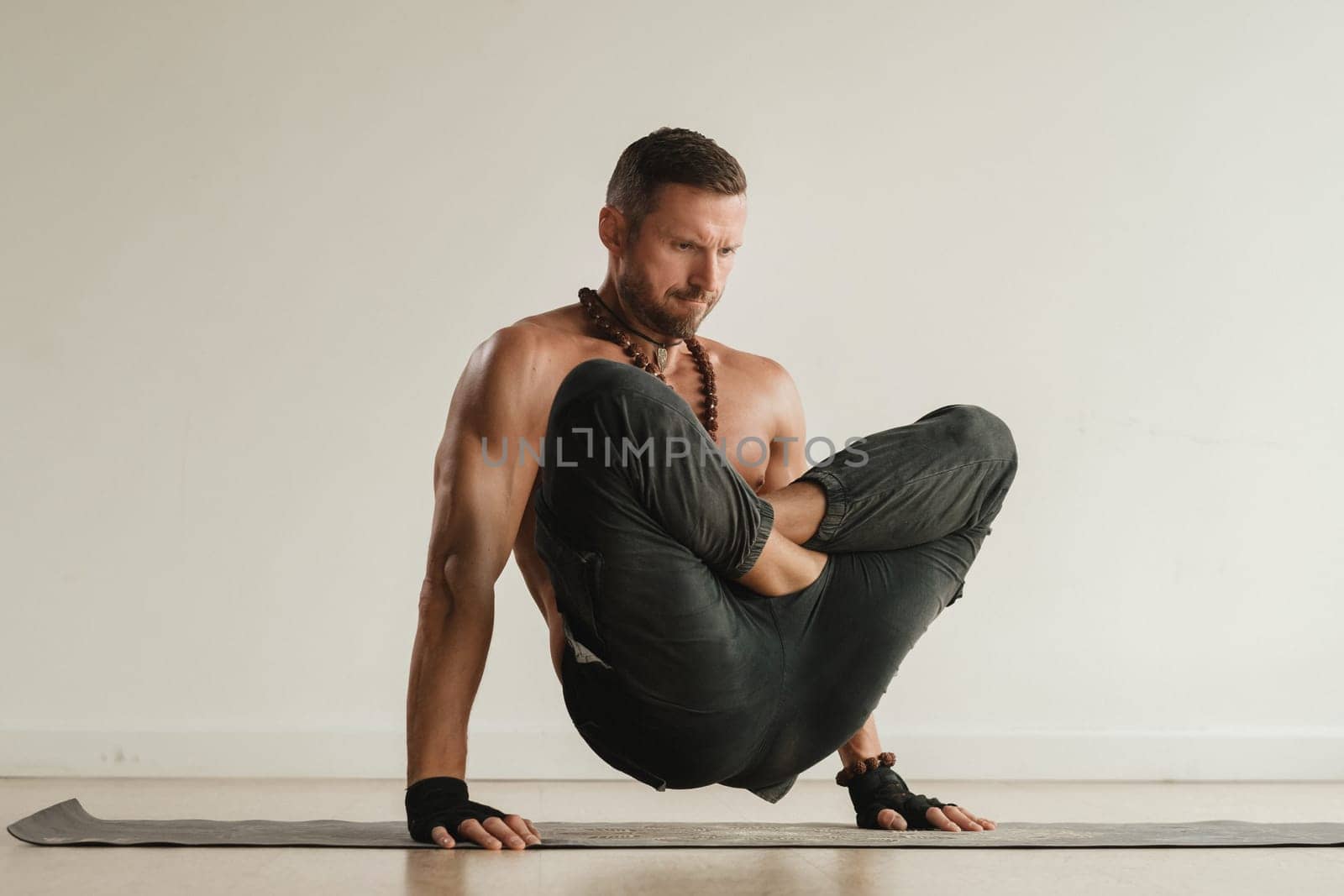a man with a naked torso does yoga standing on his hands indoors. Fitness Trainer.