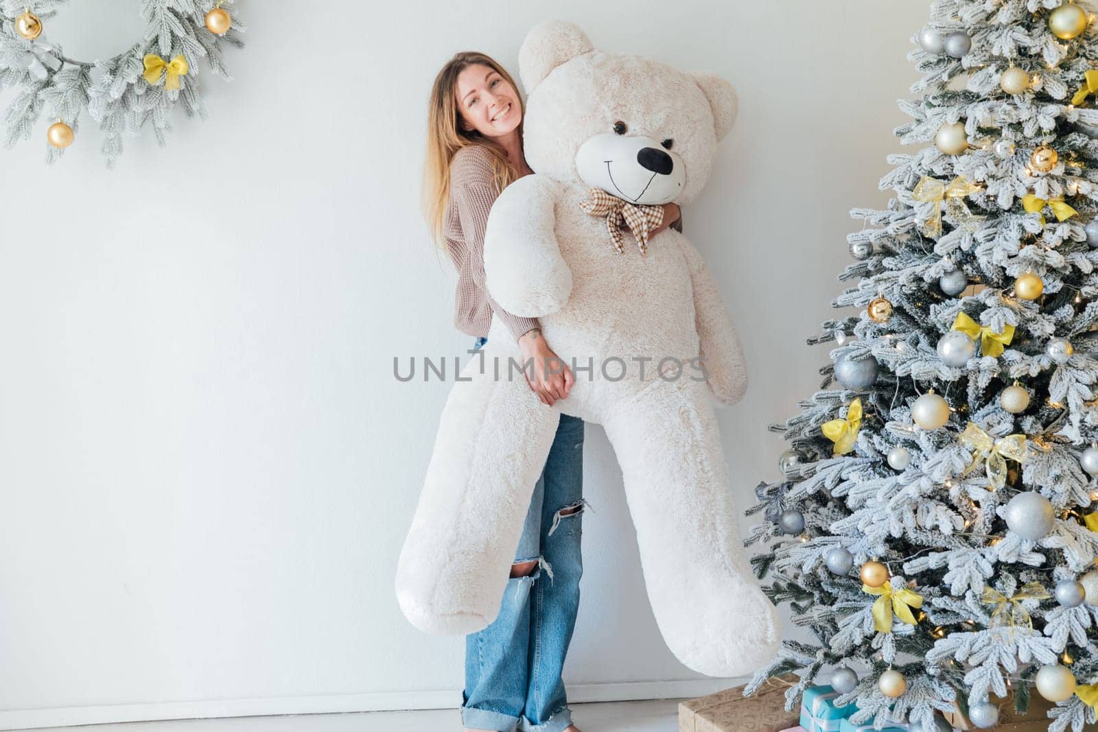 Young woman decorating christmas tree with gifts and toys by Simakov