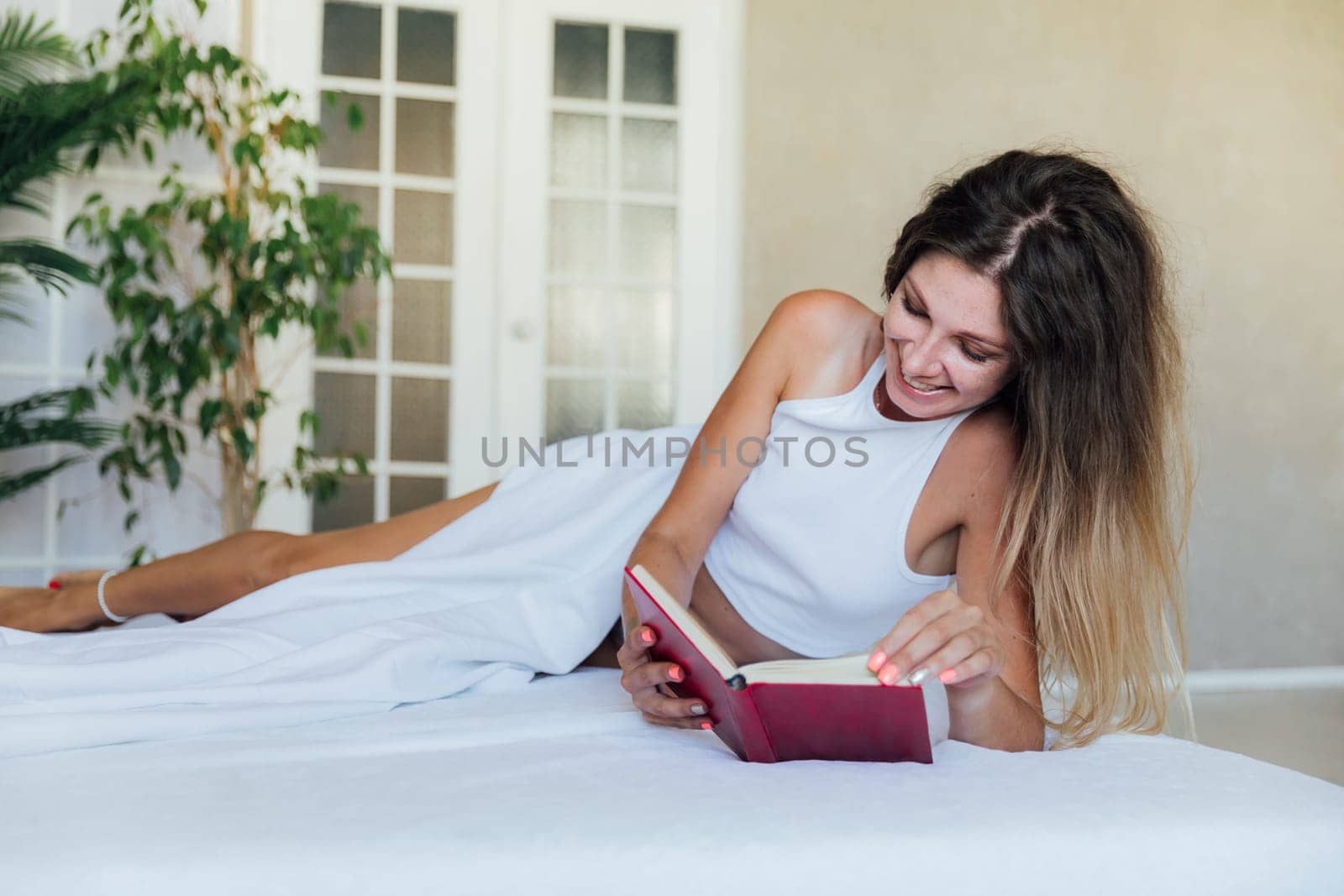 Beautiful woman in bedroom on bed reading book