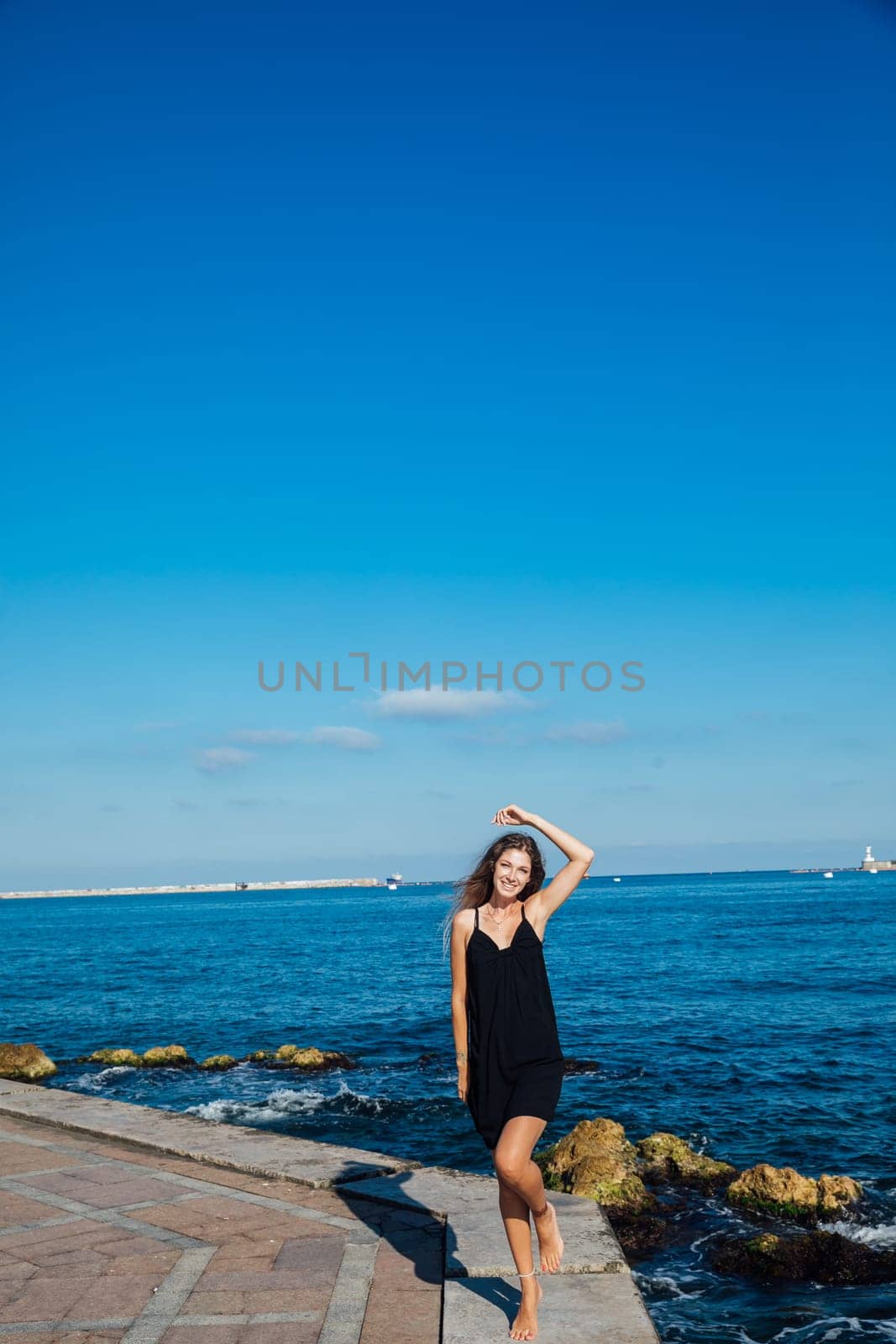 slender fashionable woman in black summer dress on a walk by the sea