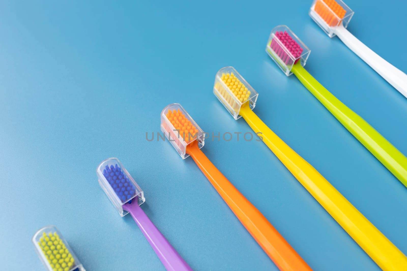 Top View Many Colorful Antibacterial Toothbrushes on Blue Background. Flat Lay Set for Dental Hygiene, Bathing Self Care Products. Horizontal Plane by netatsi